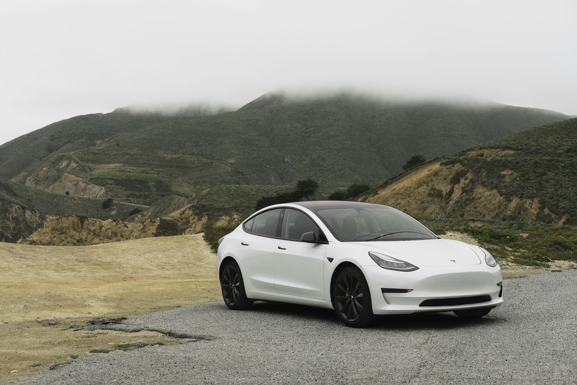 A white Tesla Model 3 parked in front of a fog-covered hillside